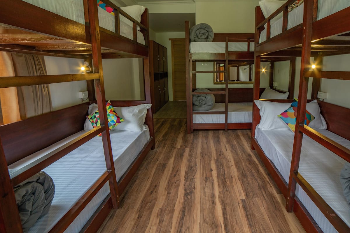 Quarto com beliches, piso de madeira e porta que dá para outro espaço.