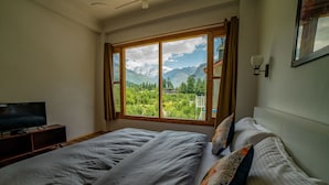 Un dormitorio con un ventanal que ofrece vistas a la montaña, una cama con almohadas estampadas y un televisor sobre un mueble.