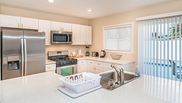 A modern kitchen with white cabinets, stainless steel appliances, a built-in oven, and a large island with a sink and dish rack. - 7 min from the strip with pool! (Las Vegas)