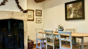 Una sala de estar acogedora con chimenea, una mesa de comedor de madera y sillas. Hay cuadros en la pared y una alfombra en el suelo.