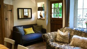 Una sala de estar acogedora con una mesa de comedor de madera, dos sofás, un espejo y una ventana con vistas a la vegetación.