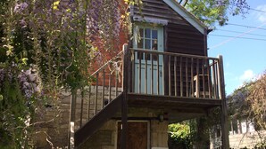 Una casa de madera rústica con un balcón, una escalera de piedra y una mesa de madera con sillas.