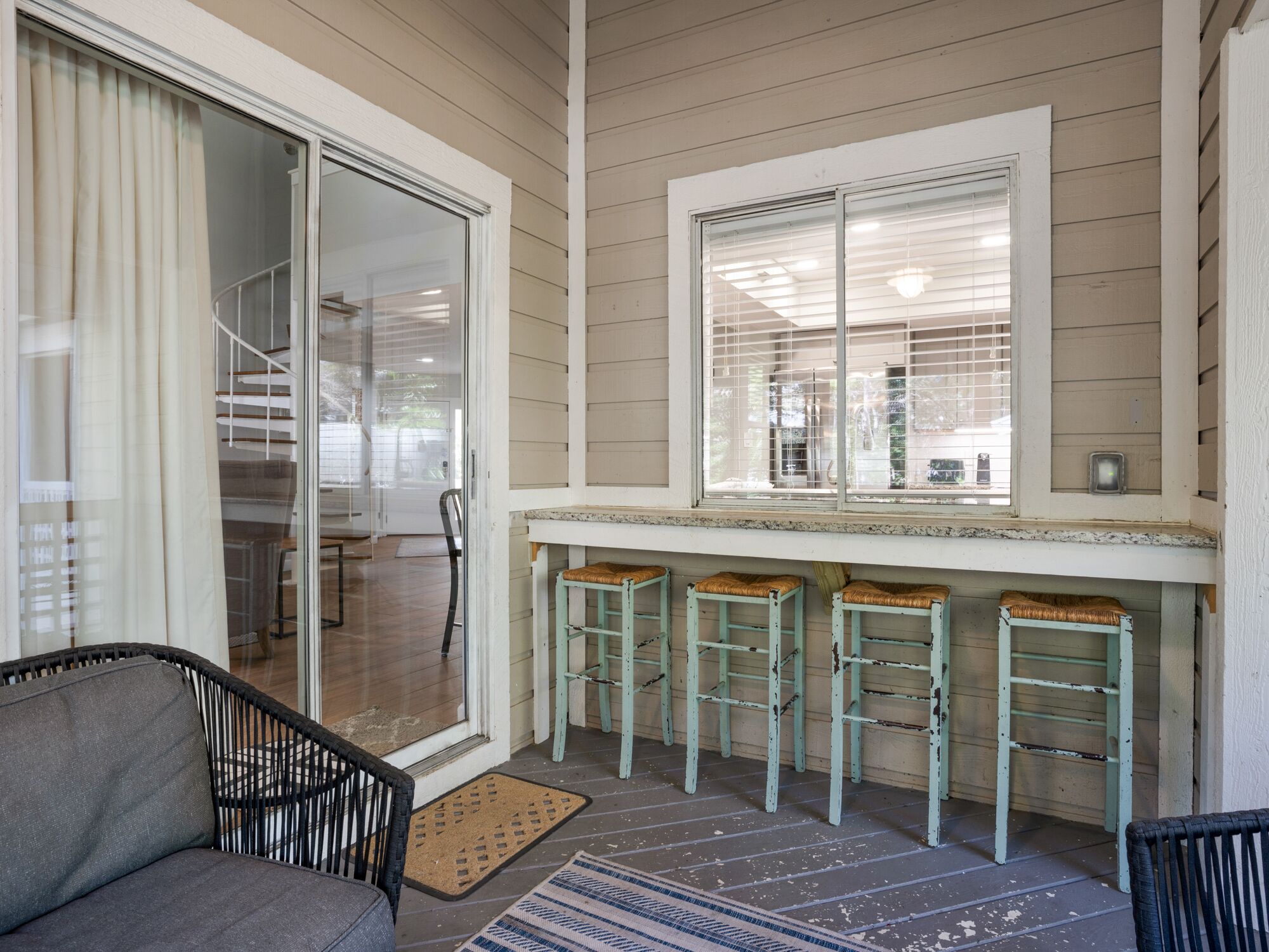 A covered porch with a sliding glass door, a small bar area with stools, and a chair.