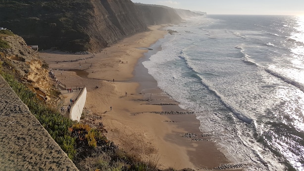 Kystlandskab med sandstrand, klipper og havbølger.