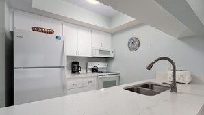 A modern kitchen with white cabinetry, a stainless steel sink, a microwave, a coffee maker, and a kettle. - Tropical Garden View 2 bed, 2 bath at Sanibel Moorings #622 (Sanibel)
