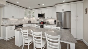 A modern kitchen with white cabinets, granite countertops, stainless steel appliances, and a central island with bar stools.
