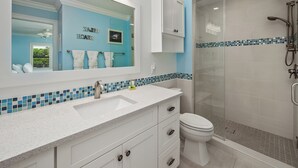 A bathroom with a white vanity, a large mirror, a toilet, and a glass-enclosed shower area.