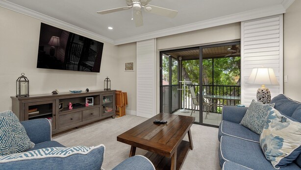 A living room with a sofa set, a coffee table, a TV mounted on the wall, and a sliding glass door leading to an outdoor area.