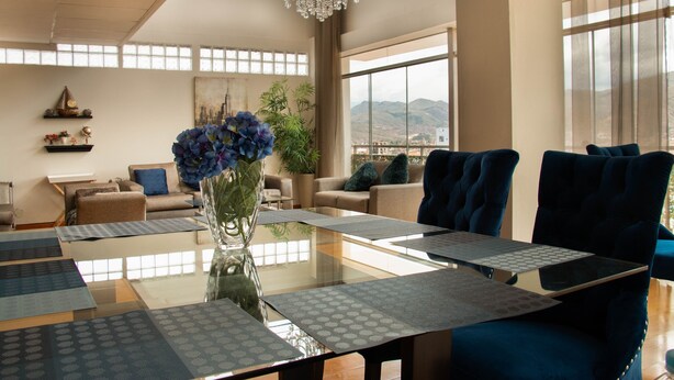 A spacious room with a large table, blue chairs, and a view of mountains through large windows. - APARTAMENTO PENTHOUSE  DE 350 M2, CON VISTA PANORAMICA DE LA CIUDAD. (Cusco)