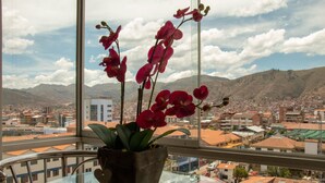 A potted orchid on a glass table with a cityscape and mountains in the background. - APARTAMENTO PENTHOUSE  DE 350 M2, CON VISTA PANORAMICA DE LA CIUDAD. (Cusco)