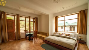 A bedroom with a large bed, a wooden desk, a chair, and a view of the outside. - Alt Life - Dharamkot - Hostel (Dharamshala)