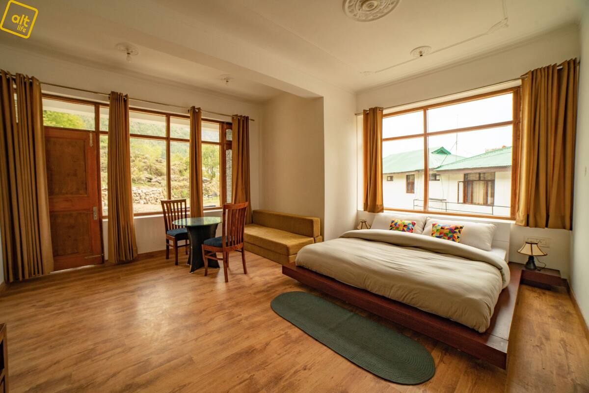 A bedroom with a large bed, a wooden desk, a chair, and a view of the outside.