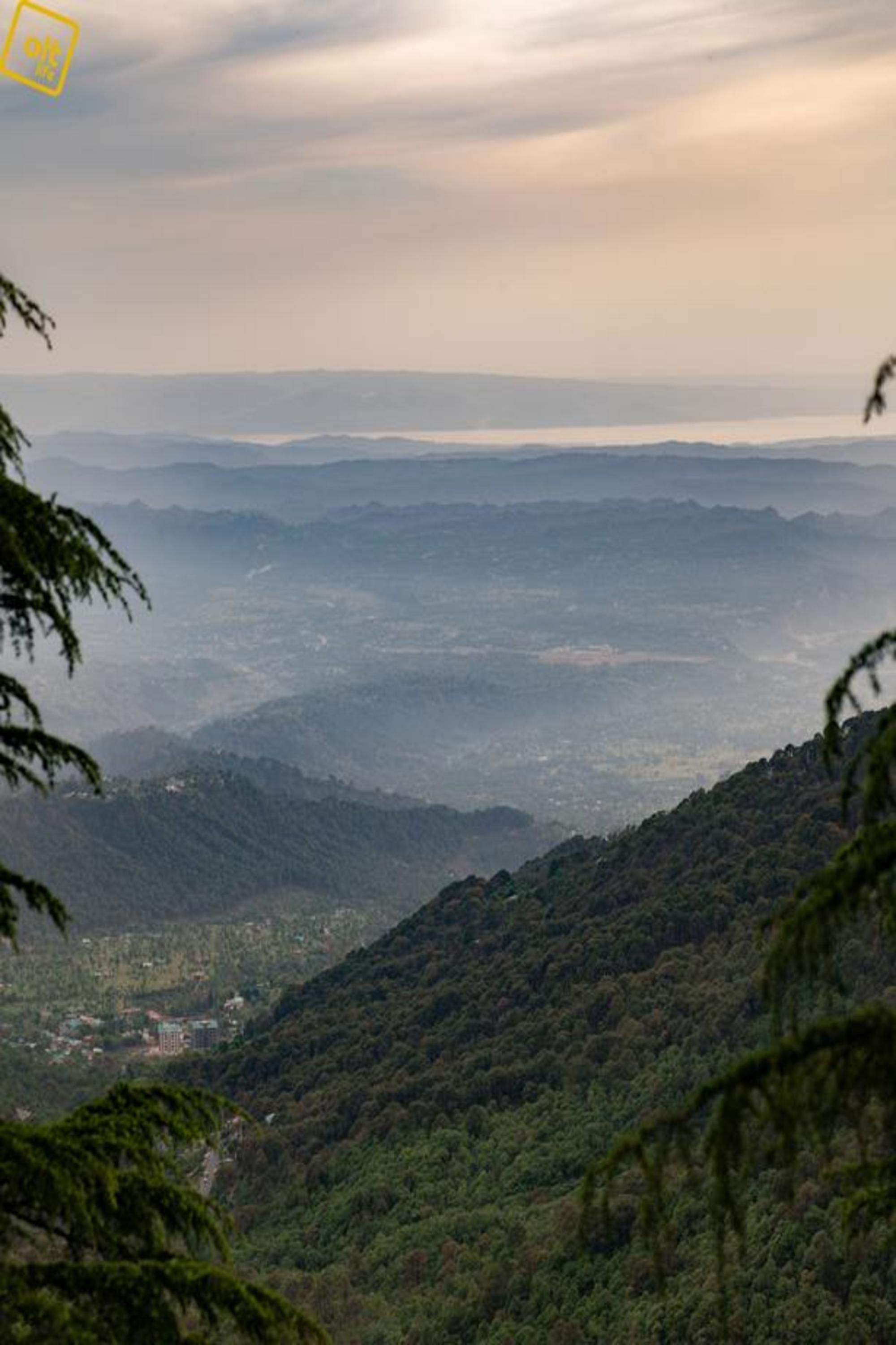Vista panorámica de un paisaje montañoso con bosques densos y una ciudad lejana.