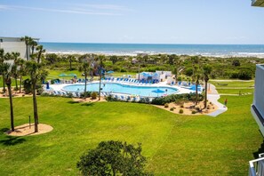A pool area with a view of the ocean, surrounded by palm trees and a grassy lawn. - CRC 1412 - Fourth Floor Condo with Beautiful Views (St Augustine)