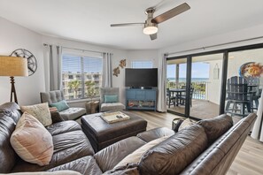 A modern living room with leather sofas, a flat-screen TV, and a balcony with outdoor furniture. - CRC 1412 - Fourth Floor Condo with Beautiful Views (St Augustine)