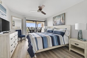 Un dormitorio con cama, escritorio, silla, ventilador de techo y ventana grande.