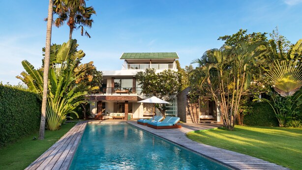 Una casa moderna con piscina, rodeada de exuberante follaje y palmeras.