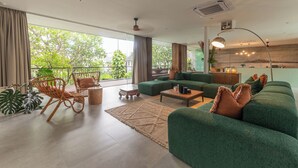 Una sala de estar moderna con un sofá verde, sillas de mimbre, una mesa de centro y vistas al exterior.