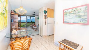 A kitchen with a glass dining table, wicker chairs, a hanging light fixture, and a view of the outdoors.