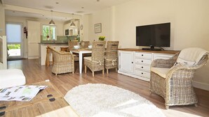 Una sala de estar moderna con un televisor de pantalla plana, muebles de mimbre y una alfombra de pelo blanco.