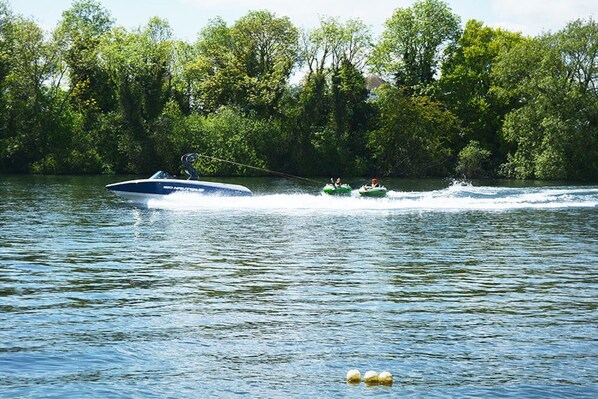 A watercraft towing two green inflatable boats on a lake surrounded by dense trees.