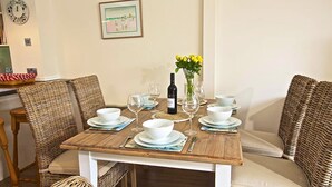 Una mesa de comedor dispuesta con platos, tazones y copas de vino, rodeada de sillas de mimbre.