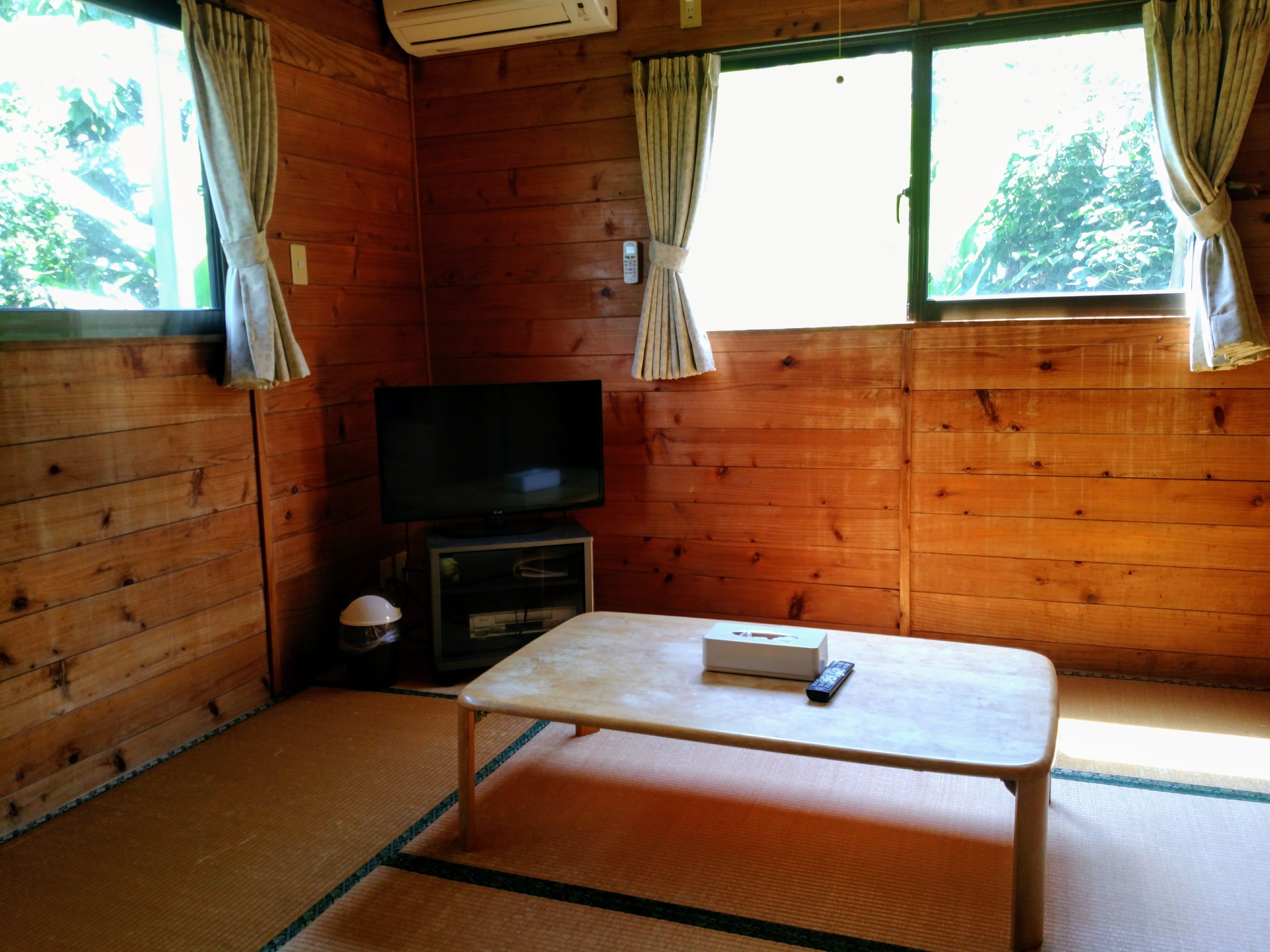 A wooden room with a television, a small table, and a window with curtains.
