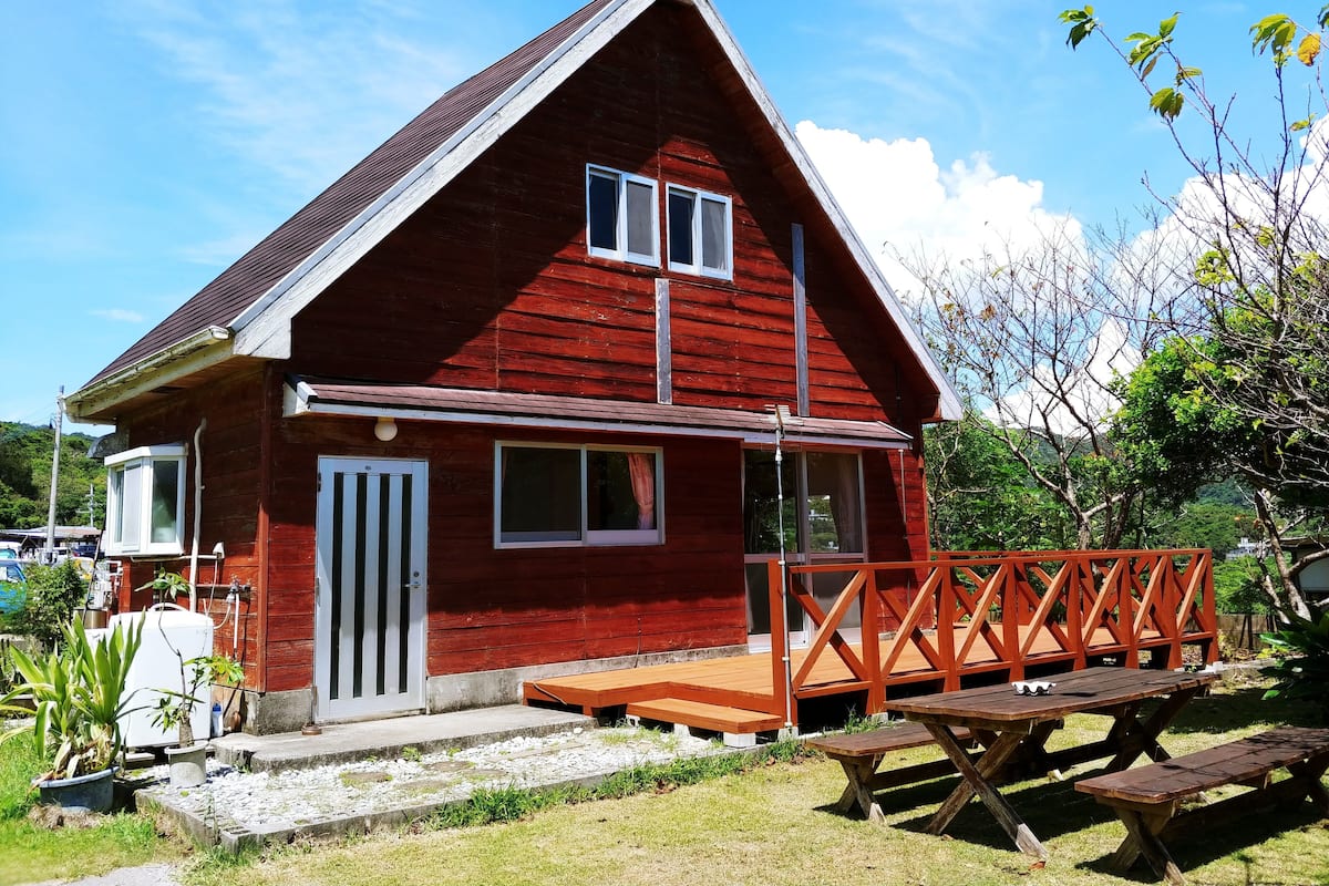 Una casa roja de madera con techo inclinado, un porche delantero y una terraza de madera.