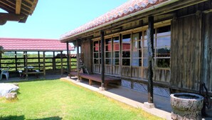 A rustic wooden building with a covered patio area, large windows, and a stone well. - Cottage CANAC (Motobu)