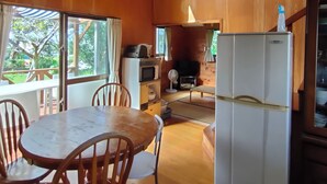 A spacious kitchen with wooden walls, a dining area with a table and chairs, and a refrigerator. - Cottage CANAC (Motobu)
