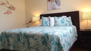 Een net opgemaakt bed met een bloemenprint sprei, twee bedlampjes en een bloemistisch kunstwerk aan de muur.