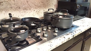 Een keuken met een gasfornuis, pannen, braadpannen en een magnetron.