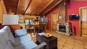 A cozy living room with a fireplace, wooden ceiling beams, a television, and a dining area. - Lorences Rural Apartments for 4 people (Somiedo)