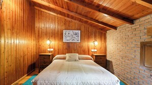 A wooden-paneled bedroom with a large bed, two bedside tables, and a brick wall. - Lorences Rural Apartments for 4 people (Somiedo)