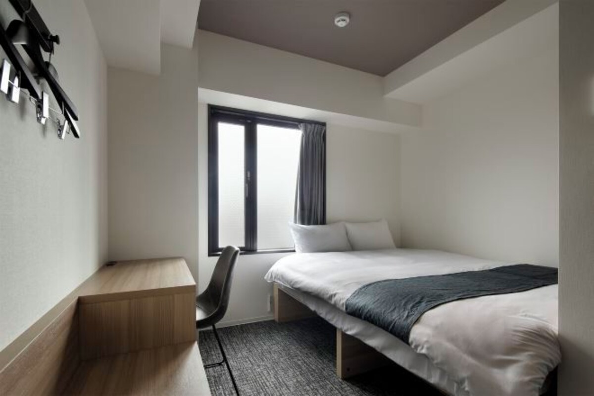 A modern hotel room with a bed, a desk, and a chair.