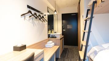 Une chambre d’hôtel avec un bureau en bois, un miroir, un lit, un lit superposé et une salle de bain équipée d’un lavabo et de produits de toilette.