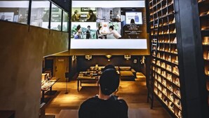 Ein modernes Interieur mit einem großen Bildschirm, der Filmszenen zeigt, Sitzgelegenheiten und Bücherregalen.