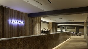 Ein Empfangsbereich mit einem 'TUNESTAY'-Schild, einer Bar mit Flaschen und einer Sitzecke mit Tischen und Stühlen.