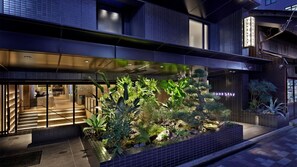 A hotel entrance with a modern design, featuring a large glass facade, a staircase leading to the entrance, and a well-maintained outdoor garden with various plants. - TUNE STAY Kyoto (Kyoto)