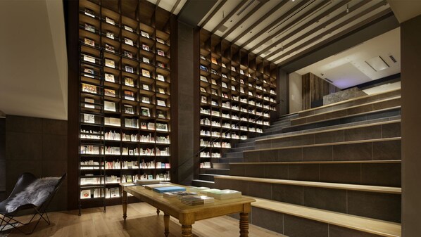A modern library interior with bookshelves, a wooden table, and a staircase.