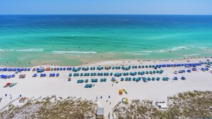 Ein Strand mit Reihen von Sonnenschirmen und Liegestühlen, ein sandiger Uferstreifen und das Meer im Hintergrund.