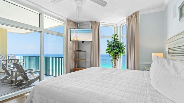 Ein Hotelzimmer mit einem großen Bett, einem Fernseher, einem Balkon mit Sitzgelegenheiten und Meerblick.