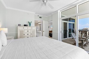 Ein Schlafzimmer mit einem großen Bett, einem Schminktisch, einem Nachttisch, einem Deckenventilator und einer Glastür zum Balkon mit Gartenmöbeln.