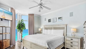 Ein Schlafzimmer mit Bett, Nachttischen, Deckenventilator, Fernseher, Pflanze und Meerblick.