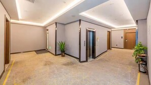 Un hall d’entrée spacieux, doté d’un sol à motifs géométriques, d’un ascenseur central et d’une plante en pot.