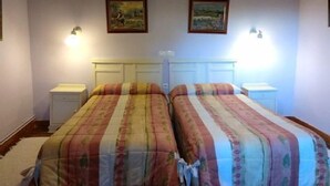 A bedroom with two beds, each with a matching headboard and bedside tables. There are two wall-mounted lamps on either side of the beds.