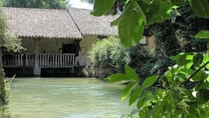 A traditional house with a tiled roof and a small balcony, surrounded by greenery and a calm water body.