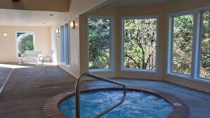 A hot tub with a metal rail, surrounded by large windows with a view of greenery. - Promo! Three Bedroom Oceanfront Condo, Wifi, HDTV, Hot Tub and Indoor Pool (Depoe Bay)