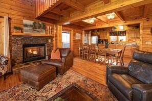 A cozy log cabin interior with a stone fireplace, leather furniture, and a dining area. - W/C Accessible, Firepit, Private, Mtn Views, Hot Tub, Pool Table (Sevierville)