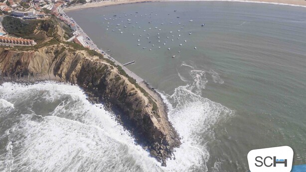 An aerial view of a coastal town with a beach, boats, and rocky cliffs. - Clérigo - T2 Holiday Apartment in São Martinho do Porto By SCH (São Martinho do Porto)